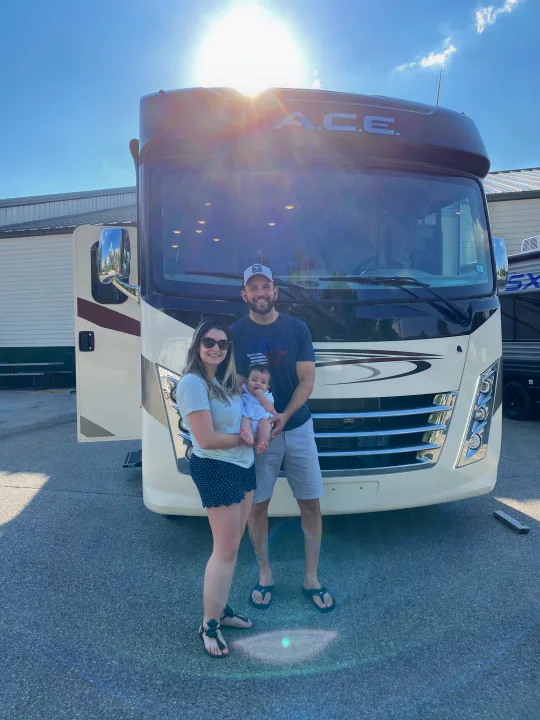 A beaming family (parents and baby) pose in front of their large rv rental, ready for new adventures.. Thor A.C.E 2020