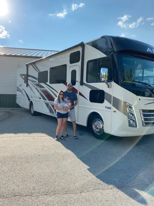 Family with baby posing proudly by their new Thor ACE RV rental, a large white motorhome. Adventure awaits!. Thor A.C.E 2020