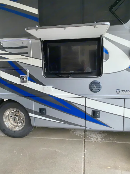 Explore this RV rental! Side view of a modern recreational vehicle showing an open outdoor TV, speaker, and utility compartments.. Thor Motor Coach Citation 2018