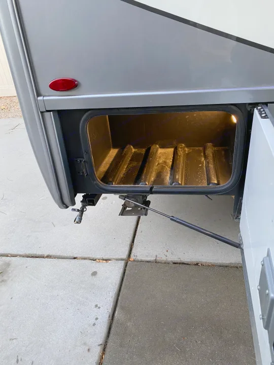 Open storage compartment of an RV rental, revealing a lit interior, gas strut, and exterior details like a red tail light.. Thor Motor Coach Citation 2018