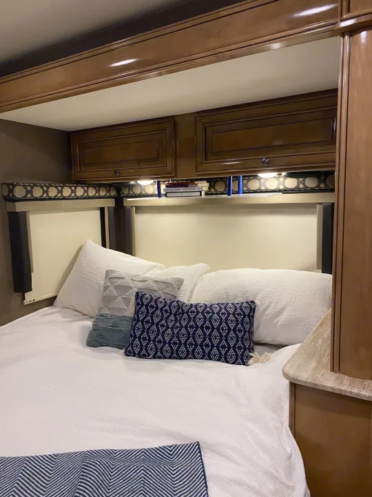 Cozy RV rental bedroom featuring wood cabinetry, bright lighting, a plush bed with white linen, and decorative pillows.. Thor Motor Coach Citation 2018
