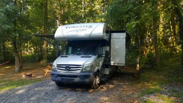 Silver rv rental Class C motorhome parked at a shady campsite with slide-out and awning extended for camping.. Forest River Forester 2018