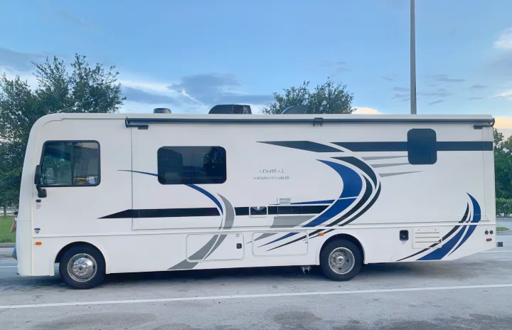 White Holiday Rambler Admiral RV rental parked on asphalt under a partly cloudy sky, featuring blue and gray graphics.. Holiday Rambler Admiral 2021