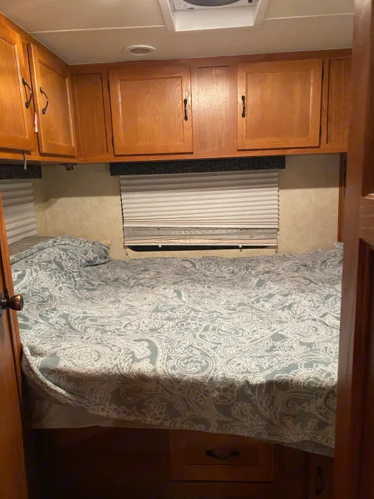 Inside an RV rental bedroom: light wood cabinets, white ceiling, and a blue/white paisley bedspread. Compact and functional.. Coachmen Freelander 2012