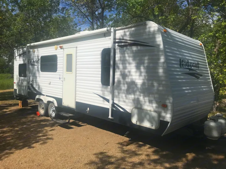 Scenic RV rental: A white travel trailer parked at a wooded campsite, ready for your next outdoor adventure.. Keystone Hideout 2009