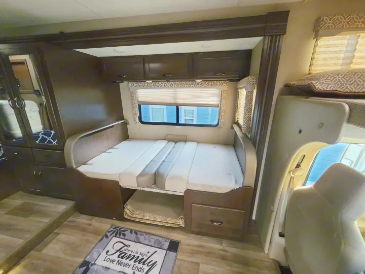 Cozy RV rental interior features a convertible bed/dinette, overhead cabinets, and a "Family" floor mat.. Thor Freedom Elite 2019