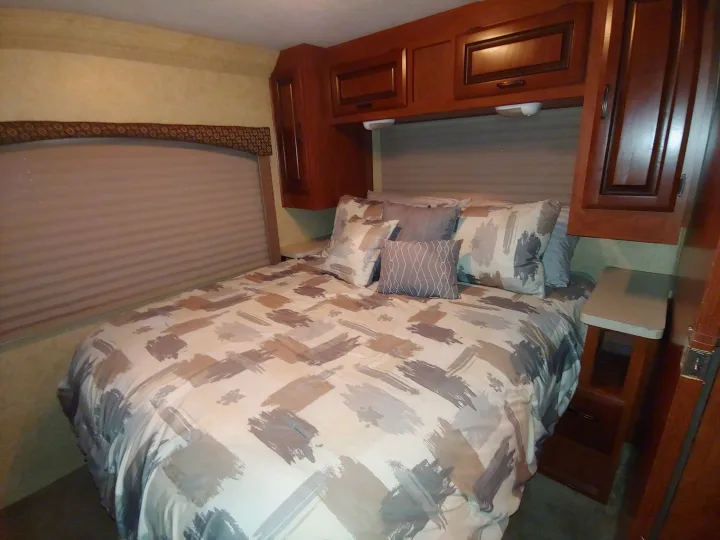 Comfort in this RV rental bedroom! Features a large bed with modern bedding, plush pillows, window blinds, and spacious cabinets.. Forest River Sunseeker 2012