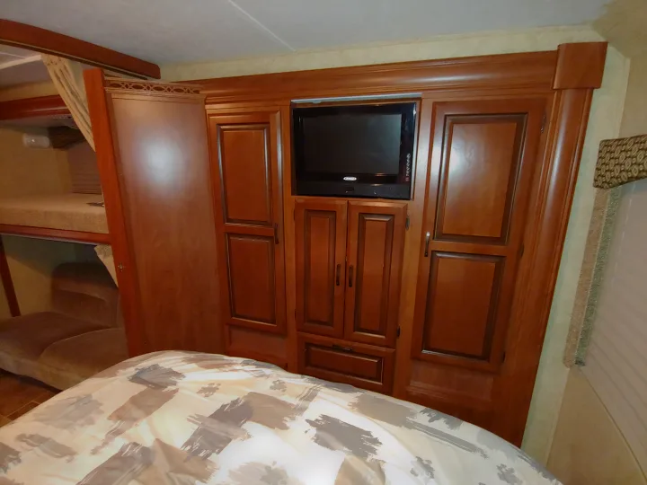 RV rental bedroom: a comfortable space with patterned bed, extensive wood cabinetry, built-in TV, and bunk beds.. Forest River Sunseeker 2012