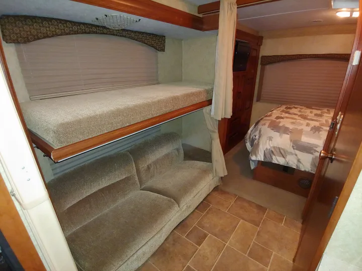 This RV rental interior features bunk beds, a sofa, and a main bedroom with a patterned comforter, optimizing compact living space.. Forest River Sunseeker 2012