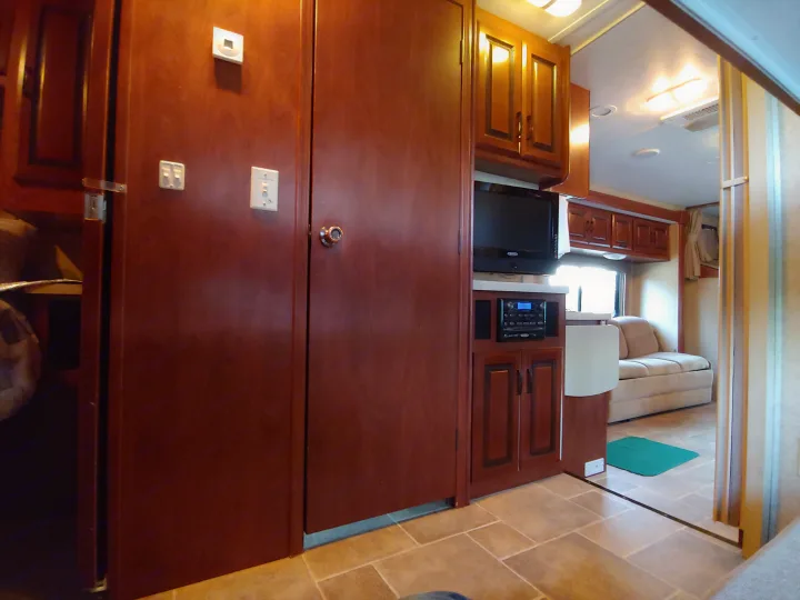Cozy RV rental interior featuring wooden cabinetry, a wall-mounted TV, and an entertainment system, with a sofa visible beyond.. Forest River Sunseeker 2012