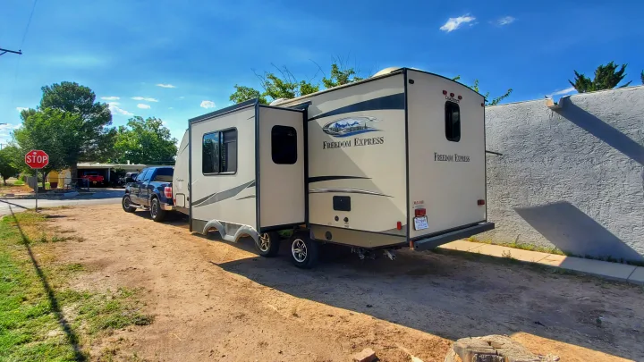 Beige Freedom Express RV/travel trailer, with a slide-out, towed by a blue truck. Consider this RV rental for your next trip!. Coachmen Freedom Express 2015