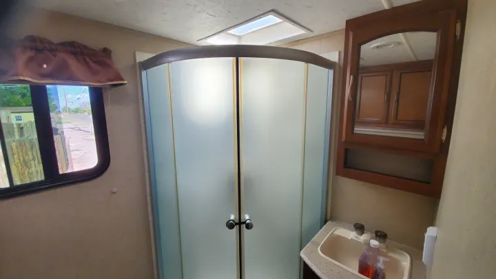 Bright RV rental bathroom with a curved frosted shower, sink vanity, and window, designed for comfortable travel.. Coachmen Freedom Express 2015