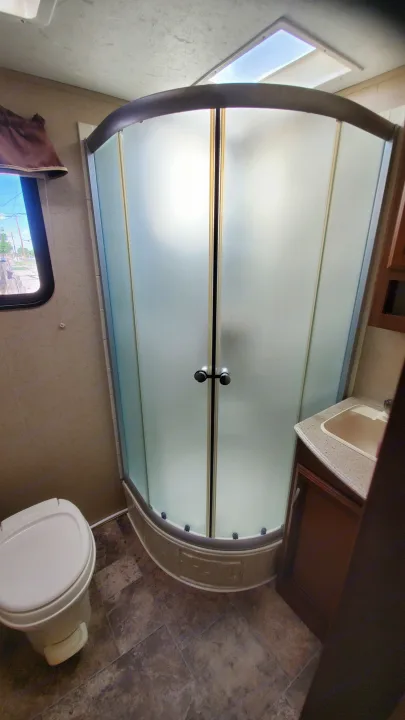 Explore this clean RV rental bathroom, featuring a corner shower with frosted glass doors, toilet, and sink vanity.. Coachmen Freedom Express 2015