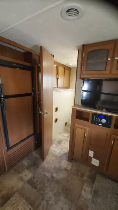 RV rental interior: A compact living/kitchen area featuring a refrigerator, TV, audio system, and ample storage cabinets.. Coachmen Freedom Express 2015