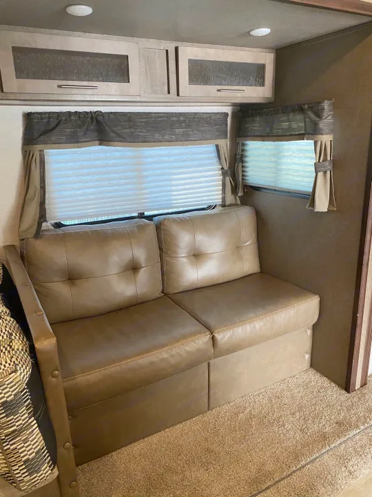 Inviting rv rental interior shows a tan sofa, pleated window blinds, wood-look cabinets, and carpeted floor.. Forest River Surveyor 2018