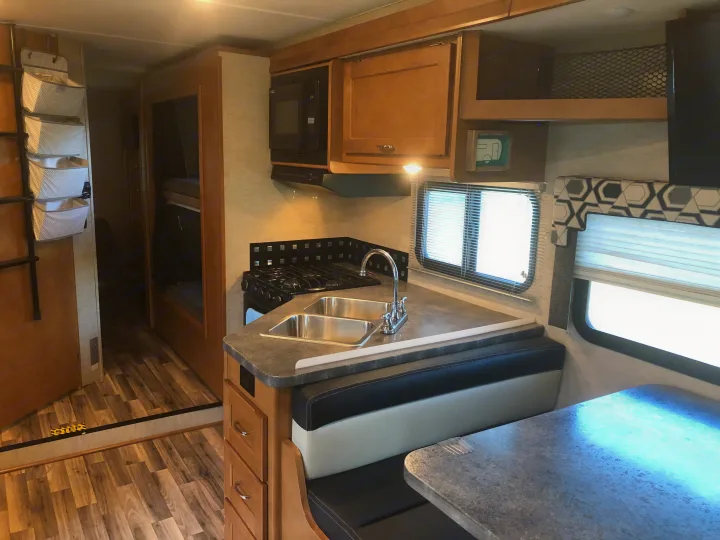 Bright RV rental interior: well-equipped kitchen (sink, stove, microwave), dinette, bunk beds, and storage.. Winnebago Minnie Winnie 2017