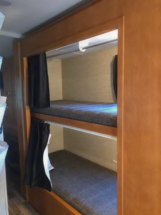 Cozy RV rental bunk beds, featuring gray mattresses and black privacy curtains, nestled in a light wood frame interior.. Winnebago Minnie Winnie 2017