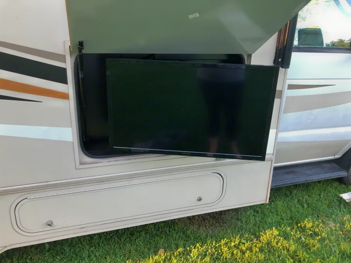 An RV rental's side storage compartment open, revealing a large TV pulled out for outdoor entertainment on grass.. Winnebago Minnie Winnie 2017