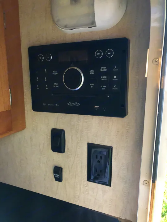 RV rental interior featuring a Jensen stereo, a water pump switch, and an electrical outlet, part of the control panel.. Winnebago Minnie Winnie 2017