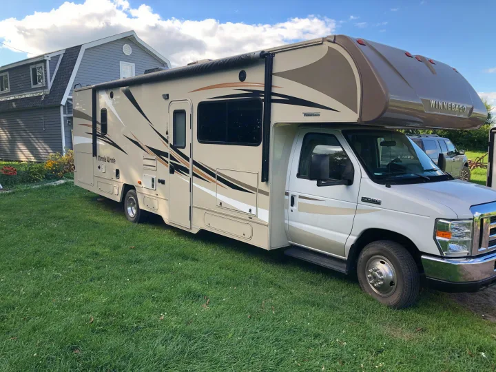 Beige Winnebago Minnie Winnie RV rental parked on grass by a house under a cloudy sky.. Winnebago Minnie Winnie 2017