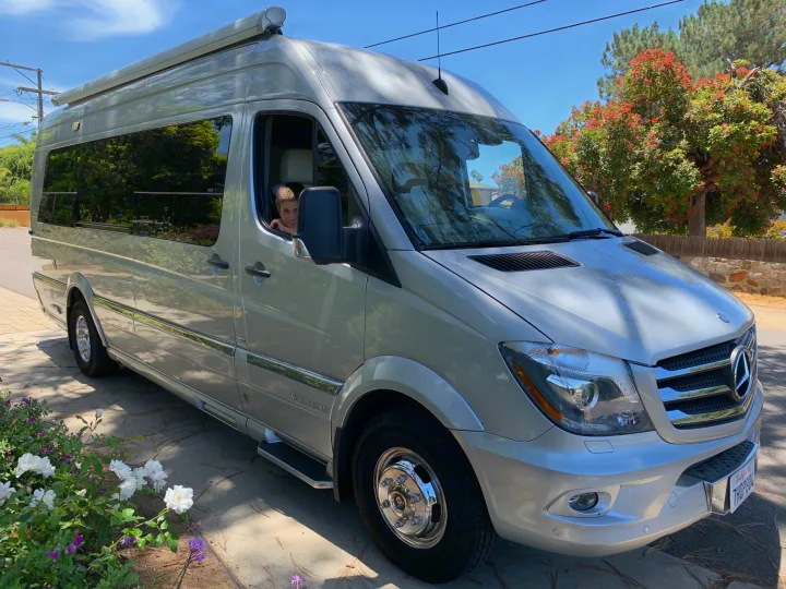 A boy looks out from a silver Mercedes-Benz Sprinter Airstream RV rental, parked on a sunny day.. Airstream Airstream 2014