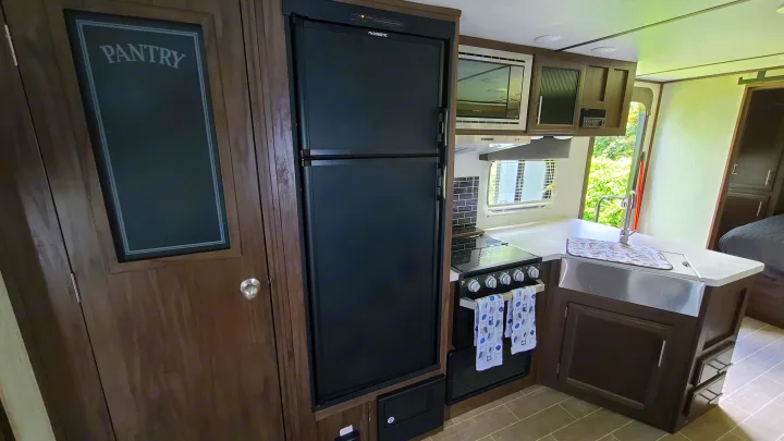Inside a cozy RV rental: Full kitchen with Dometic fridge, Furrion microwave, stove, sink & 'Pantry' cabinet.. Forest River Alpha Wolf 2020