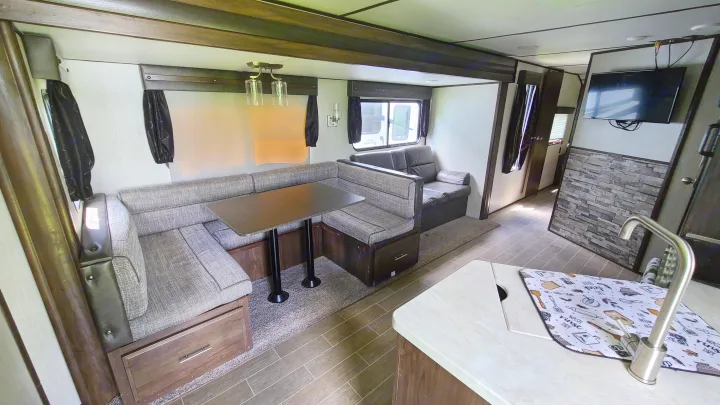 RV rental interior showing a comfortable living area with a U-shaped dinette, kitchen counter with sink, sofa, and mounted TV.. Forest River Alpha Wolf 2020