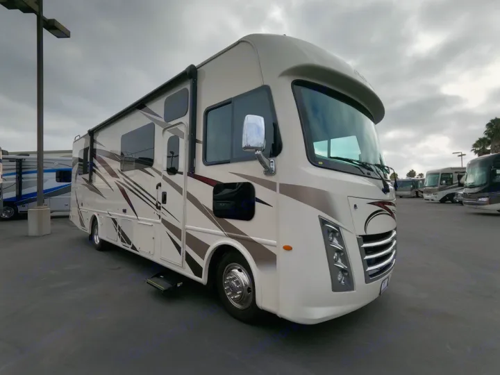 Explore options for an rv rental! This cream Class A motorhome sits on a dealership lot under a cloudy sky, with other RVs in the background.. Thor Motor Coach A.C.E 2020