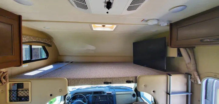 Inside an RV rental, showcasing the spacious cab-over bunk bed with mounted TV, and the driver's area below.. Thor Chateau 2019