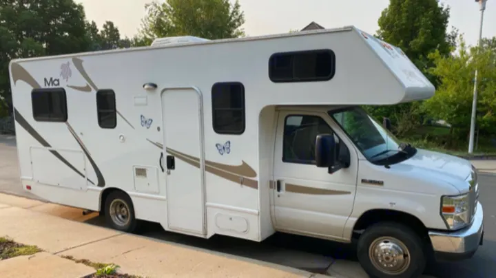 A white Class C RV, adorned with butterfly graphics and parked on a street, available for rv rental.. Thor Motor Coach Four Winds Majestic 2014
