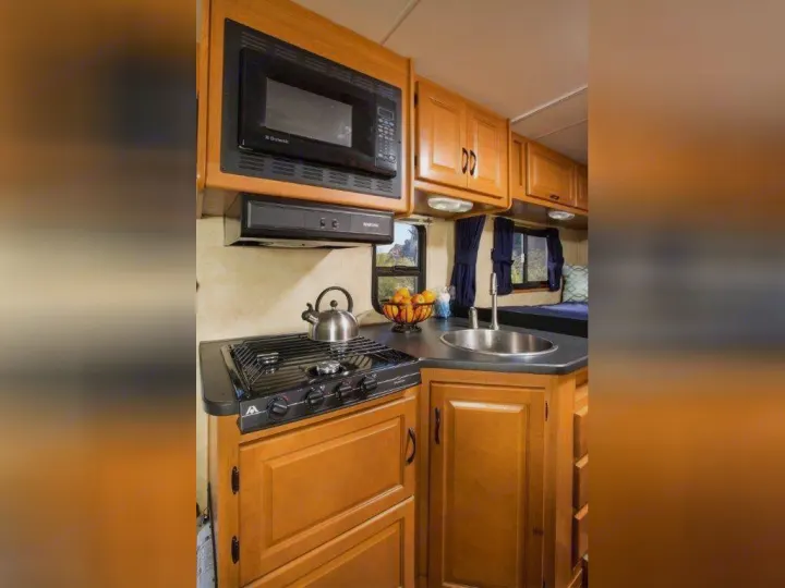 RV rental kitchen featuring microwave, stove, sink, and wooden cabinets for convenient travel cooking.. Thor Motor Coach Four Winds Majestic 2014