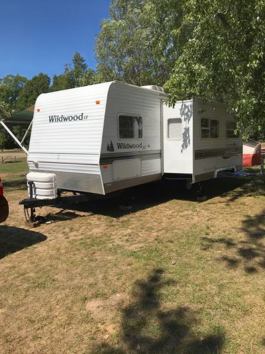 A white Wildwood LE travel trailer at a sunny campsite. Find your ideal RV rental for outdoor adventures.. Forest River Wildwood 2005
