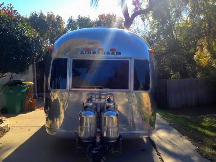 Gleaming silver Airstream RV, with propane tanks, parked on a sunny driveway. Consider for your next RV rental.. Airstream Sovereign 1973