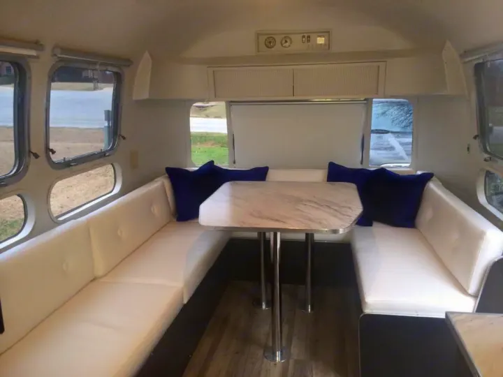 A bright, modern Airstream RV rental interior with U-shaped white seating, a marble table, and large windows.. Airstream Sovereign 1973