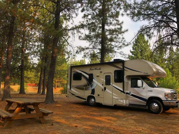 RV rental Class C camper parked among tall pine trees with a picnic table. A red caboose is visible in the background.. Other Four Winds 2018