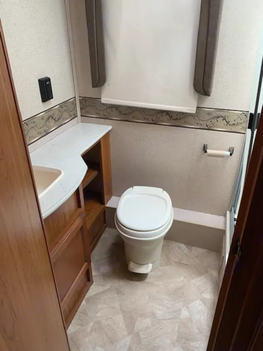 Rotated view of an RV rental bathroom, showing a white toilet, sink vanity, and adjacent compact bed/seating area.. Jayco Redhawk 31X 2017