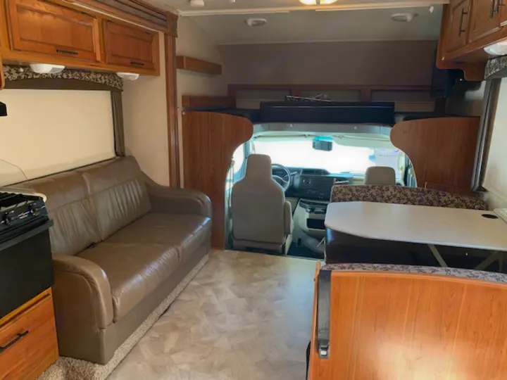Spacious rv rental interior with a brown sofa, dinette, overhead cabinets, and front driver's area visible.. Jayco Redhawk 31X 2017