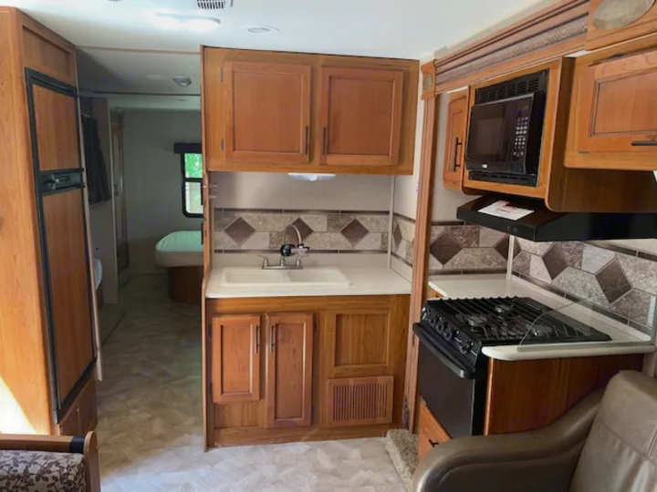 RV rental kitchen area featuring a sink, stove, microwave, and fridge. A hallway leads to a bedroom, perfect for mobile adventures.. Jayco Redhawk 31X 2017