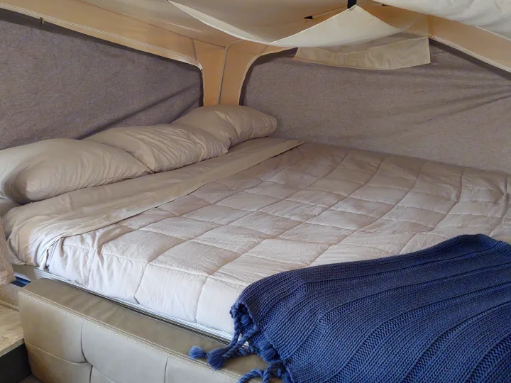 Cozy RV rental bedroom with light bedding, pillows, and a blue knitted blanket on a comfy quilted bed.. Forest River Rockwood Freedom 2021