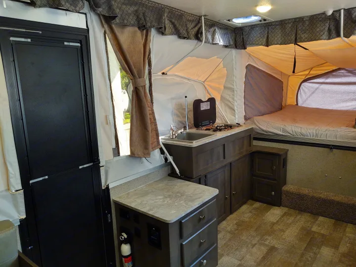 This RV rental's pop-up camper interior features a kitchen with sink/stove, cozy bed, and compact utility/storage areas.. Forest River Rockwood Freedom 2021