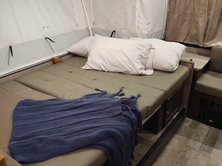 RV rental bed setup in a cozy pop-up camper, featuring plush cushions and a warm blue blanket.. Forest River Rockwood Freedom 2021