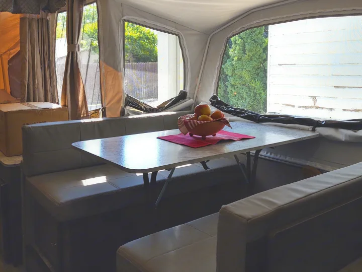 RV rental interior: cozy dinette with table, benches, and a fruit bowl. Bright windows show outside views, perfect for camper life.. Forest River Rockwood Freedom 2021