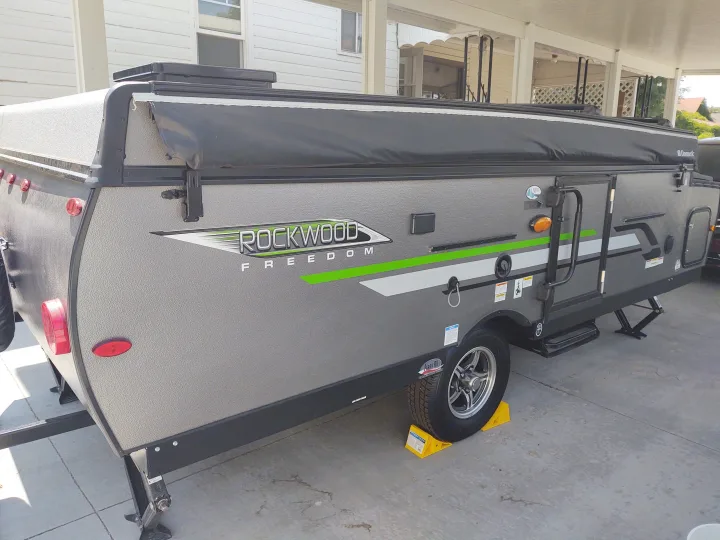 View of a gray Rockwood Freedom pop-up RV rental with Dometic awning, set up on concrete with chocks and jacks.. Forest River Rockwood Freedom 2021