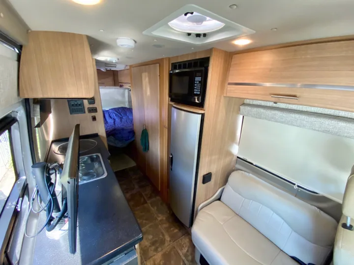 Bright rv rental interior: compact kitchen (sink, microwave), living area with sofa, and bed at the back.. Other Other 2013