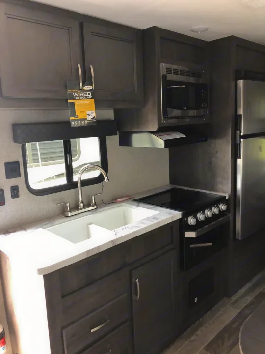 Modern RV rental kitchen with dark cabinets, white countertop, sink, stove, microwave, and fridge. Wired for solar.. Jayco Jay Flight 2021