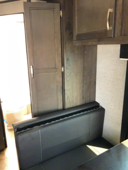 Compact RV rental interior features a black dinette, wood grain cabinets, and a bathroom entrance.. Jayco Jay Flight 2021