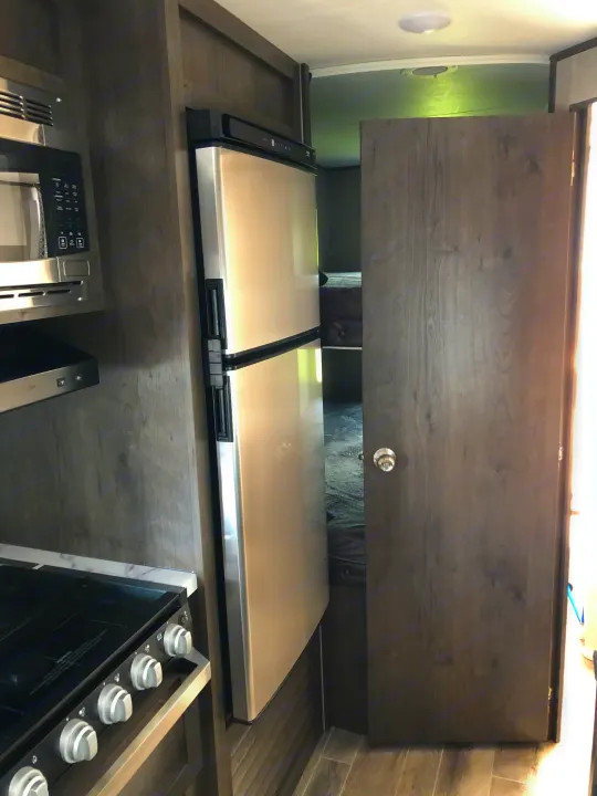 Modern RV rental interior with a kitchen (microwave, fridge, stove) and a view into the bunk bed area through an open doorway.. Jayco Jay Flight 2021