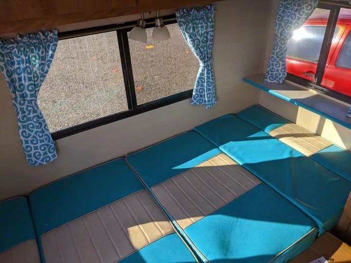 Bright RV rental interior featuring teal and tan cushions, patterned curtains, and windows with sunlight.. Gulf Stream Vintage Cruiser 2020