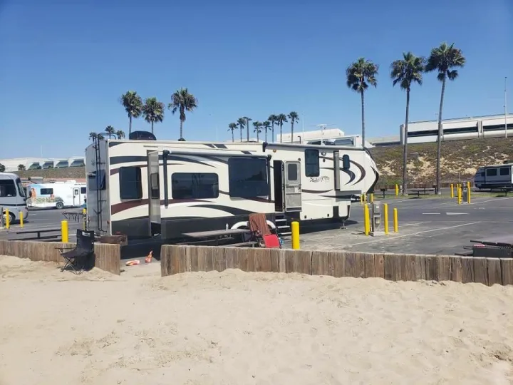 Spacious RV rental parked at a sunny beachside campground, complete with sandy access and palm trees. Great for a vacation!. Grand Design Solitude 2016