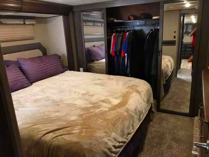 Comfortable RV rental bedroom: large bed with purple pillows, beige comforter, and built-in closet. Mirrors show the spacious interior.. Grand Design Solitude 2016